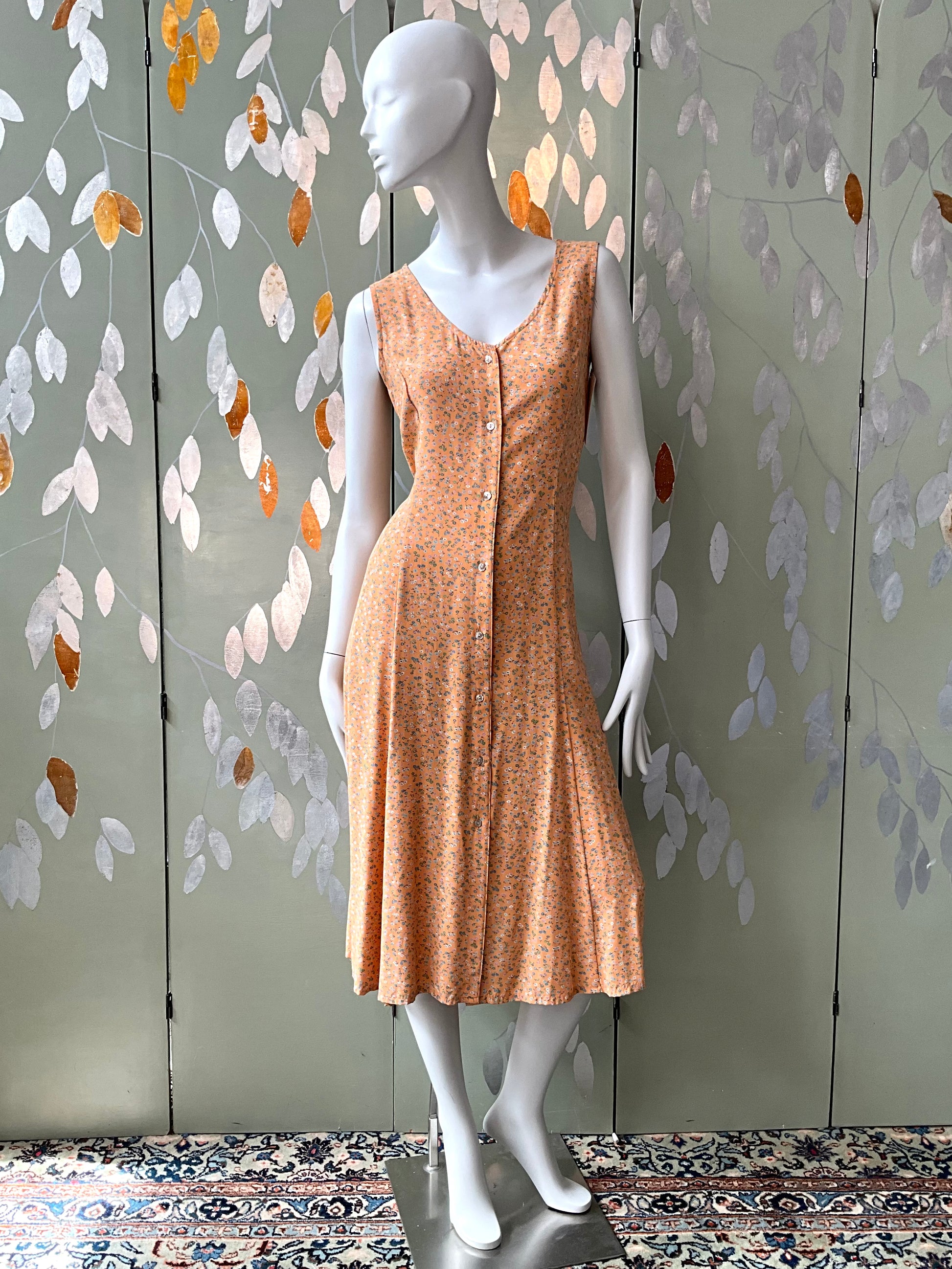 Mannequin wearing a peach dress against a decorative wall with leaf patterns.