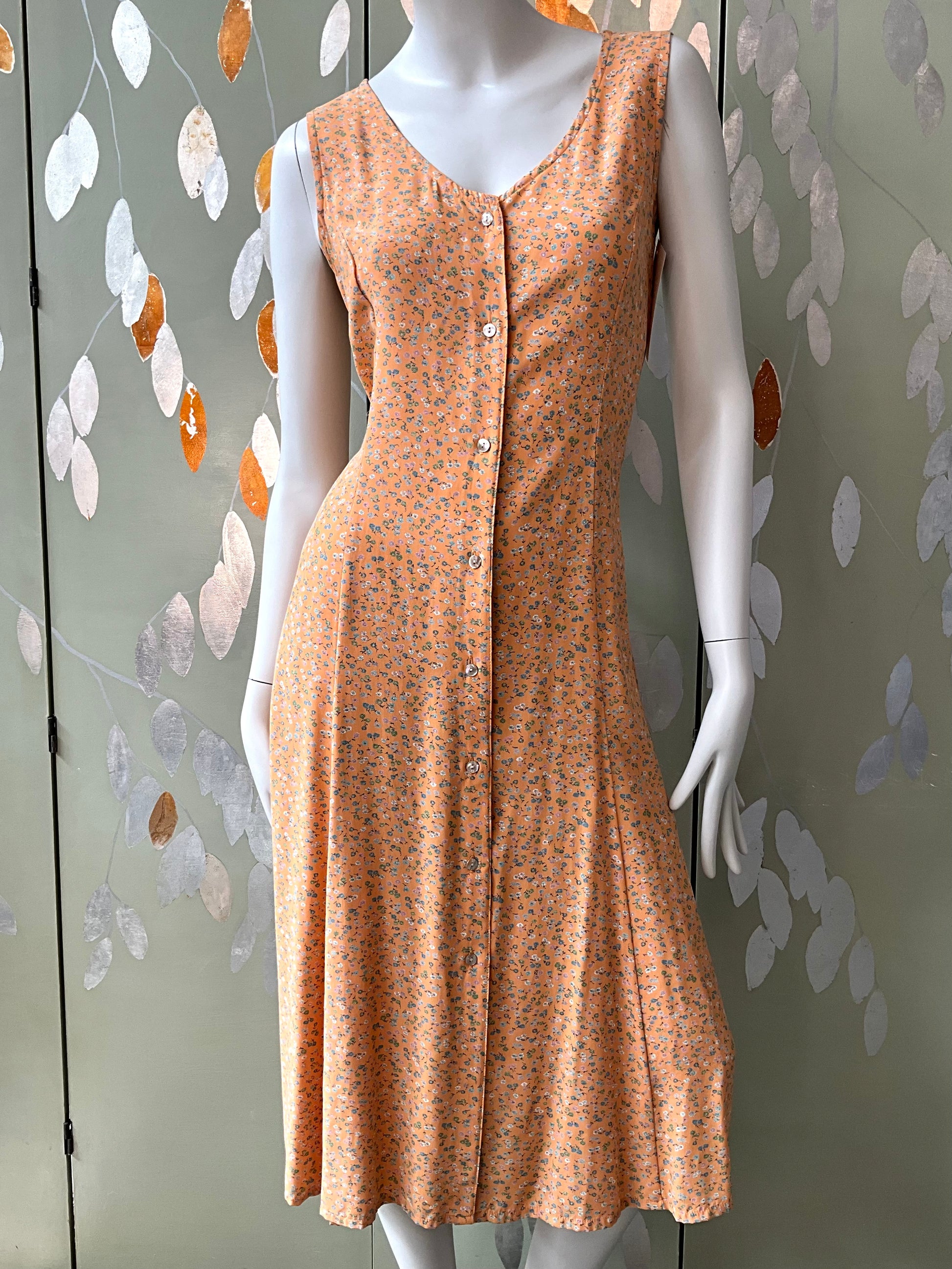 Mannequin wearing a sleeveless, button-up dress with a floral pattern against a decorative wall.