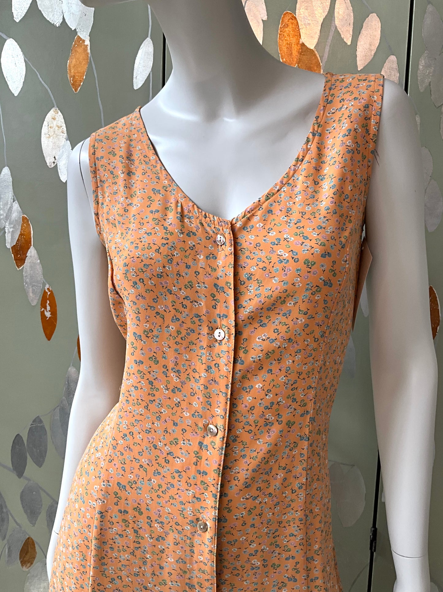 Mannequin wearing an orange floral sleeveless dress against a decorative wall.