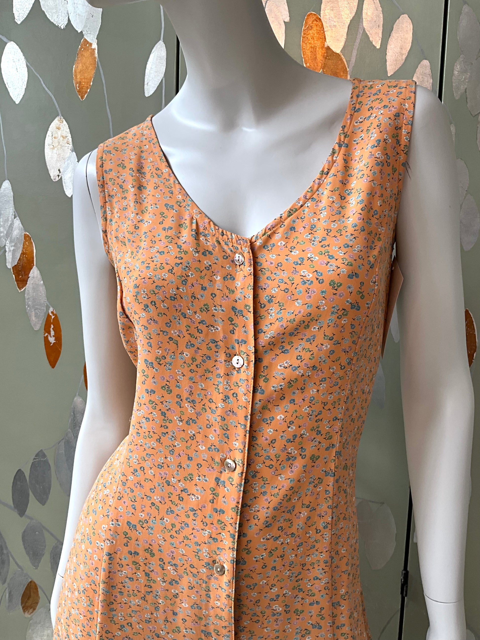 Mannequin wearing an orange floral sleeveless dress against a decorative wall.