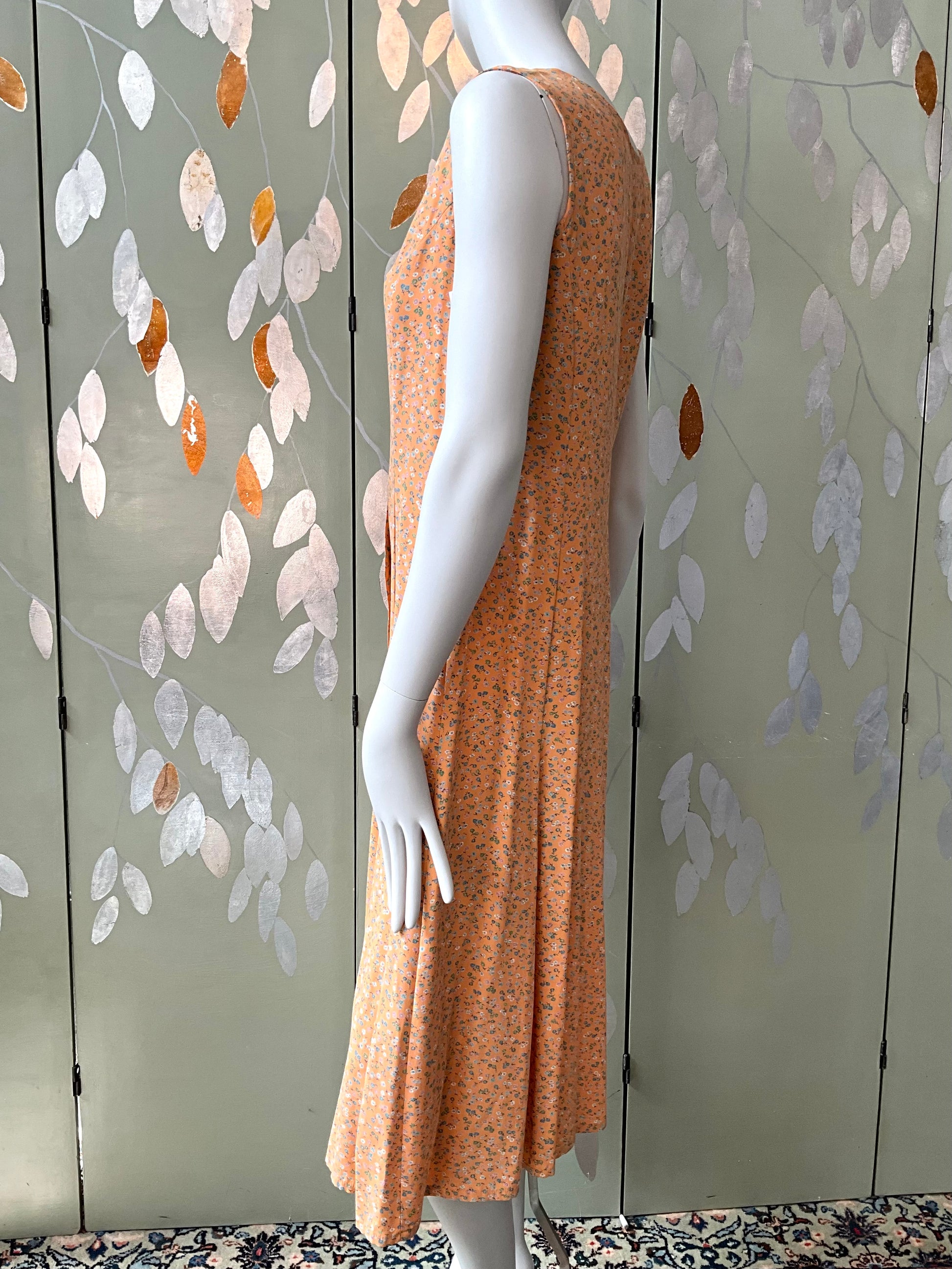 Mannequin wearing a peach dress against a decorative wall with leaf patterns.