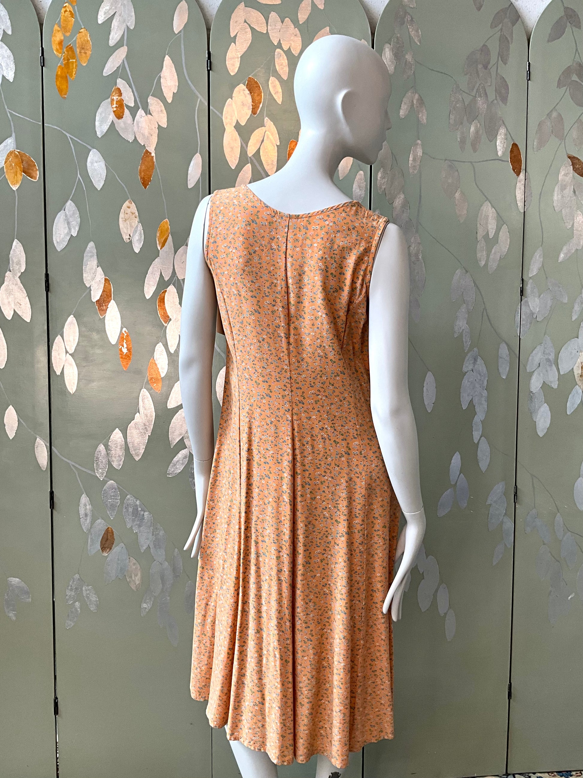 Mannequin wearing a peach dress against a decorative wall with leaf patterns.