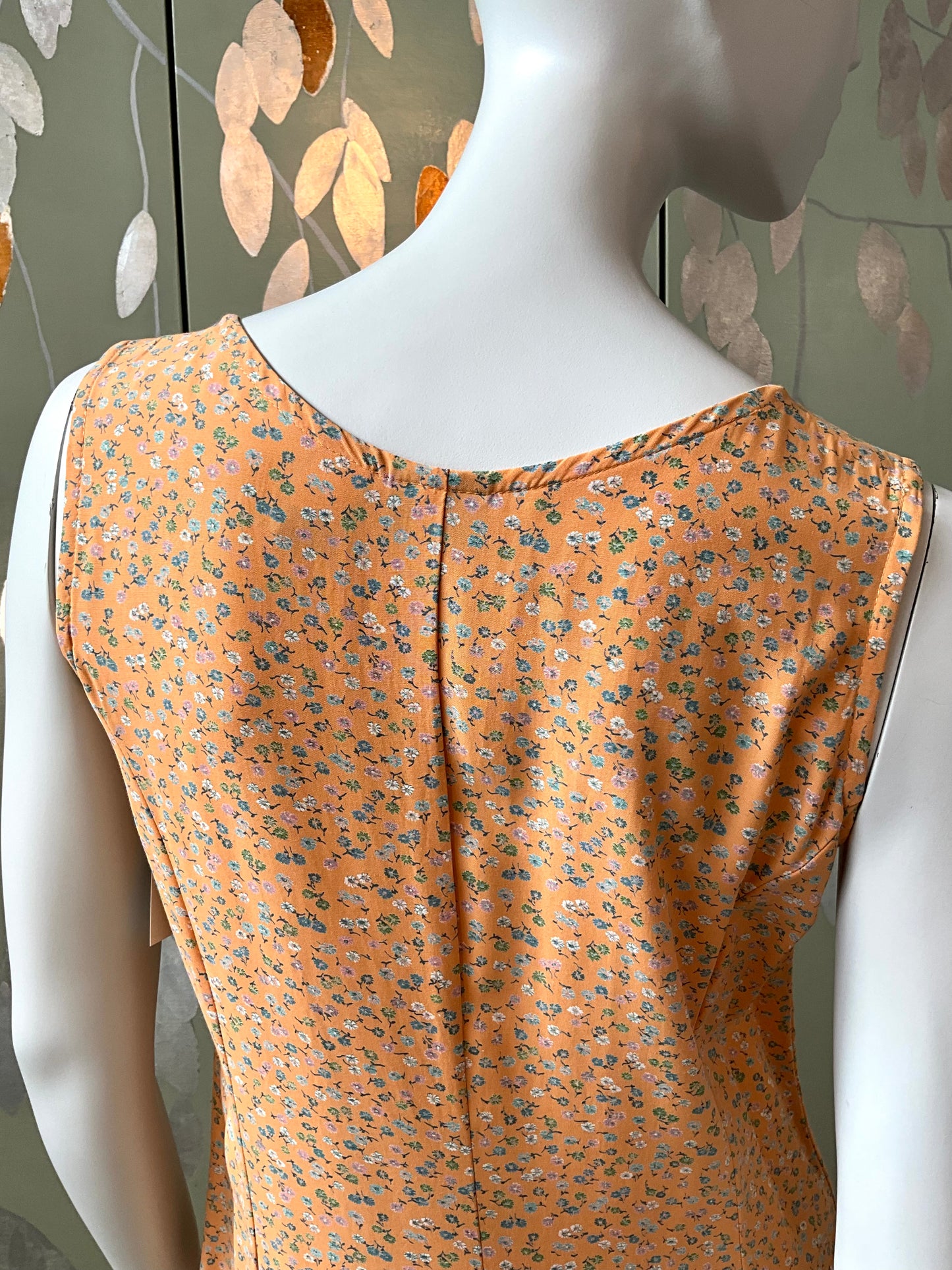 Orange floral dress on a mannequin against a decorative wall.