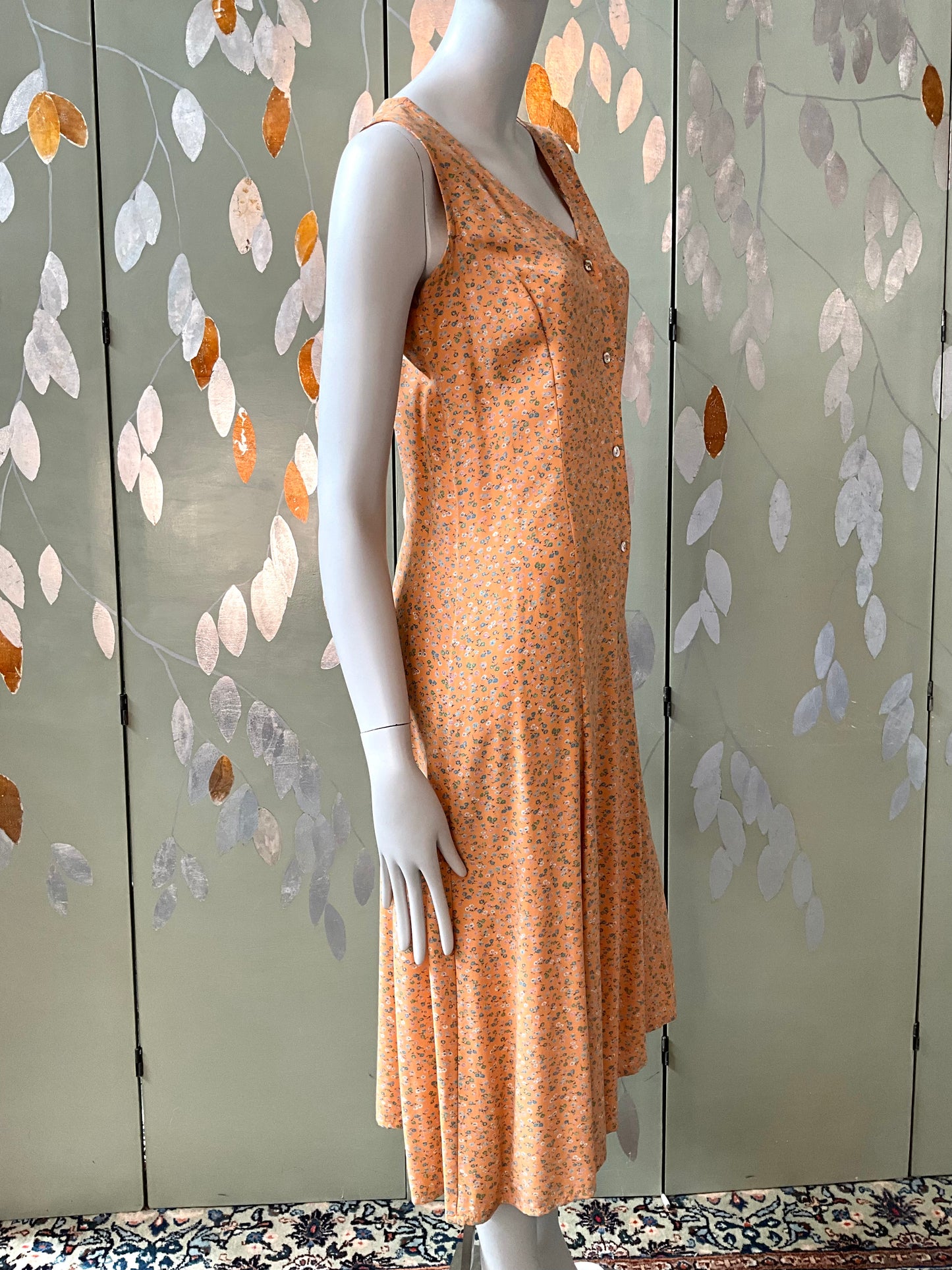 Mannequin wearing a peach-colored dress against a decorative wall with leaf patterns.