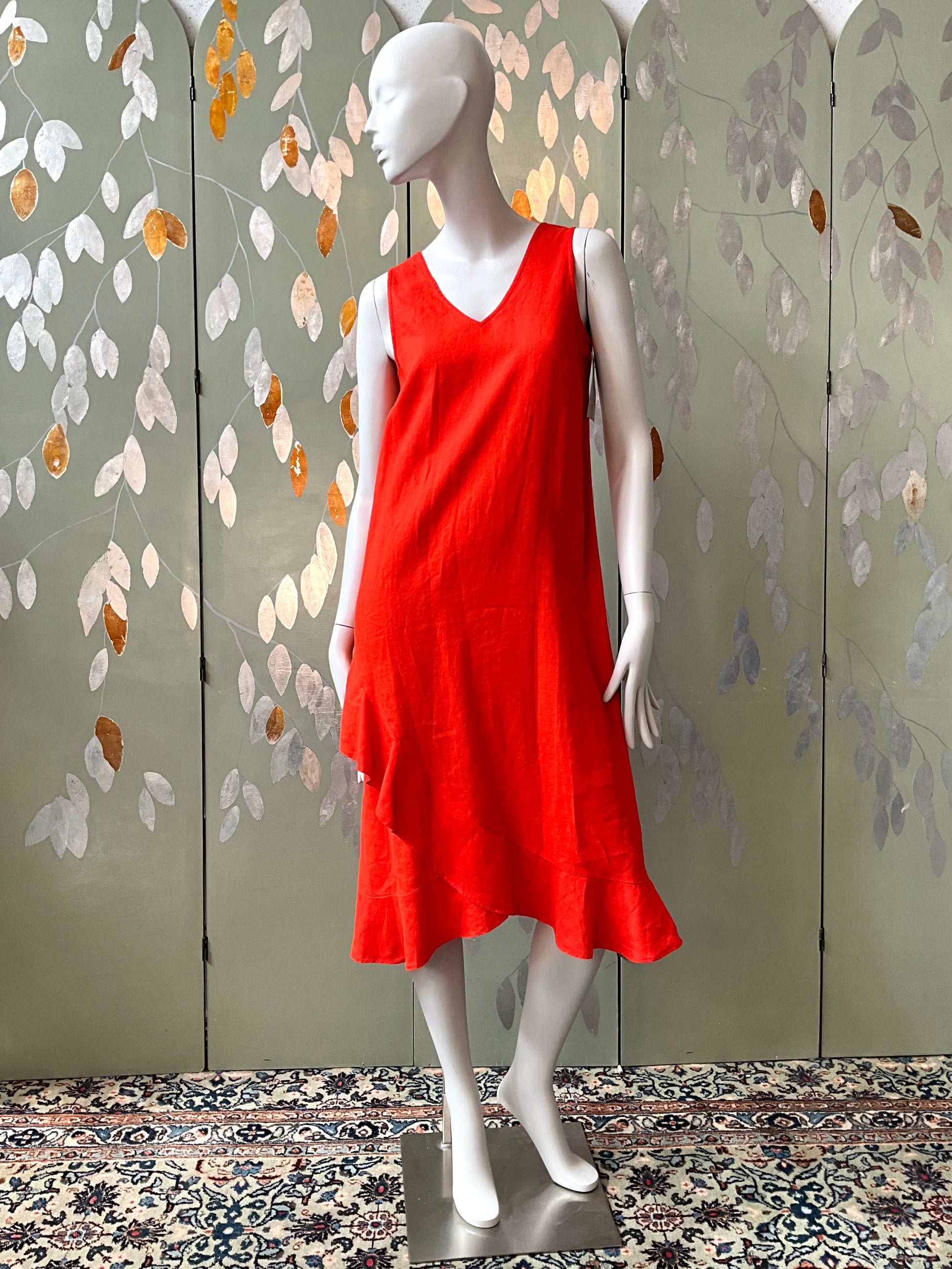 Mannequin wearing a red dress against a decorative wall with leaf patterns.