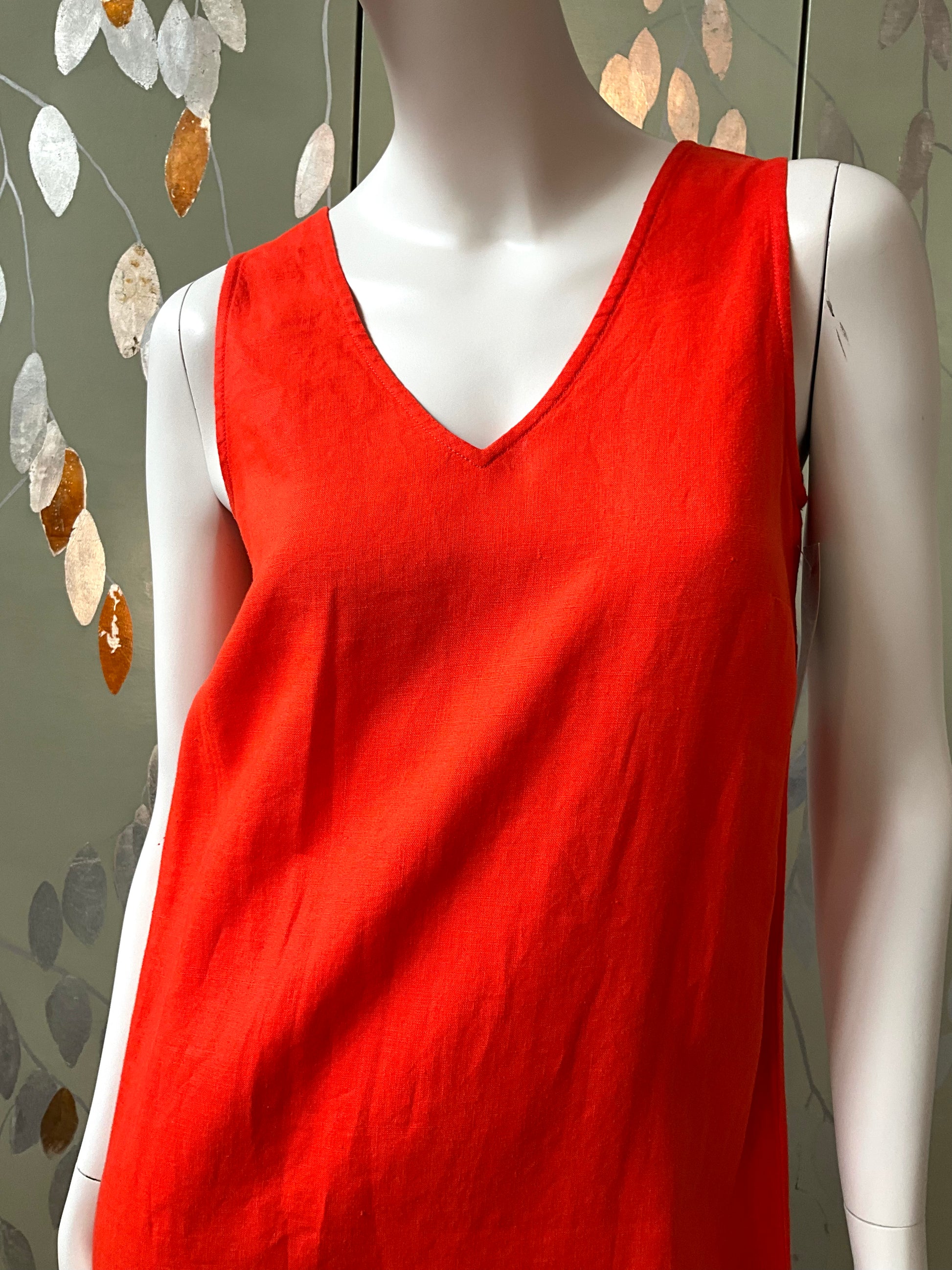 Red sleeveless dress on a mannequin against a decorative wall.
