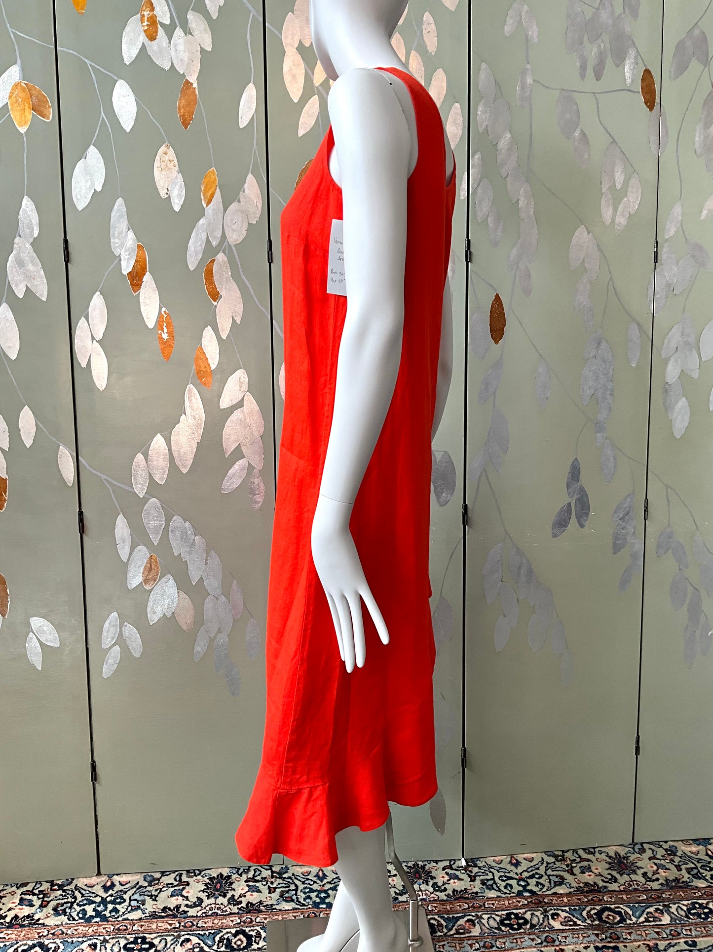 Mannequin wearing a red dress against a decorative wall with leaf patterns.