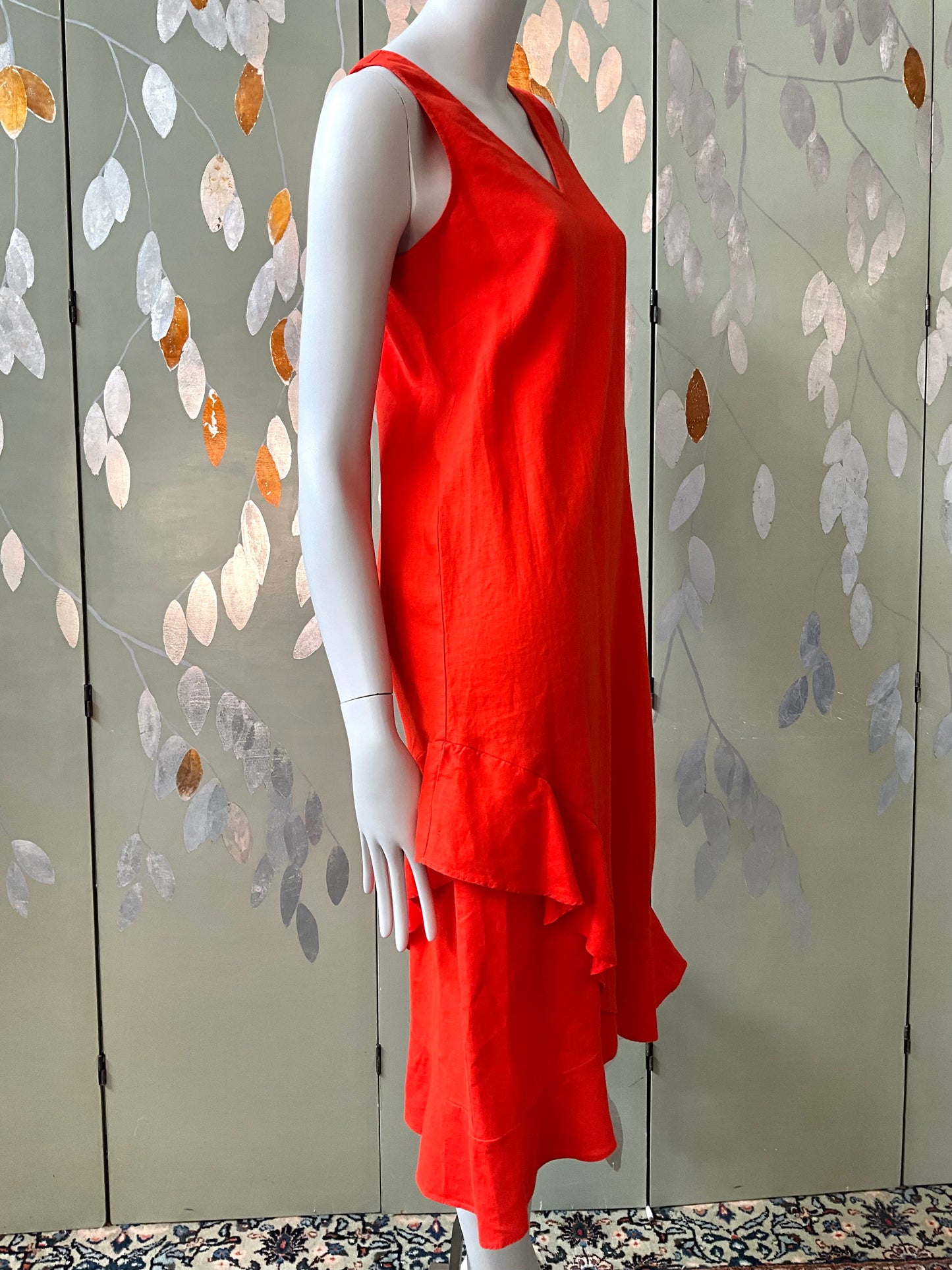 Red dress on a mannequin against a decorative wall with leaf patterns.