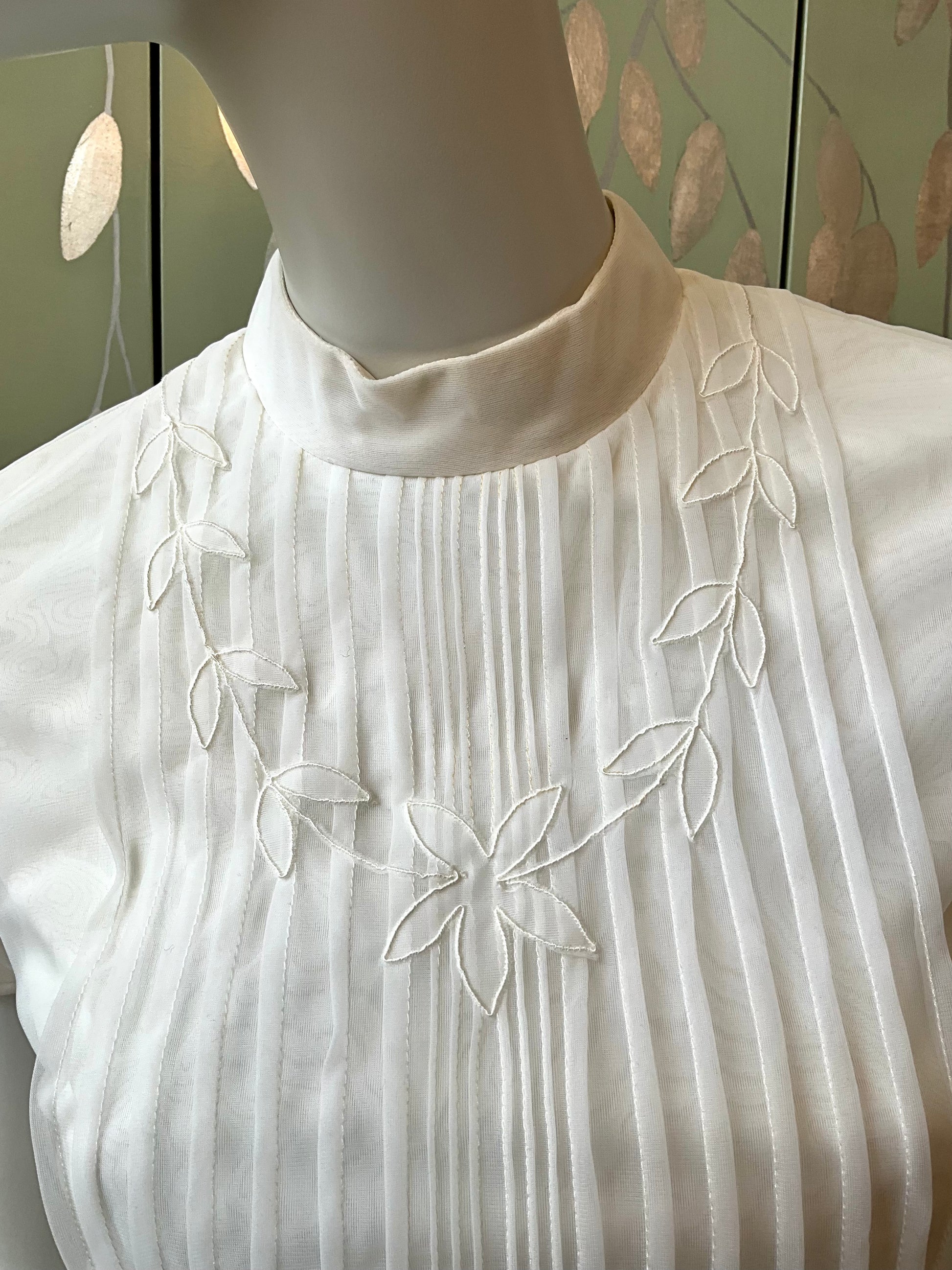 White blouse with floral embroidery on a mannequin against a neutral background