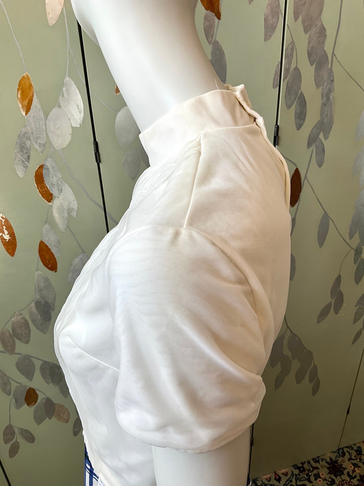 White shirt on a mannequin against a decorative wall.