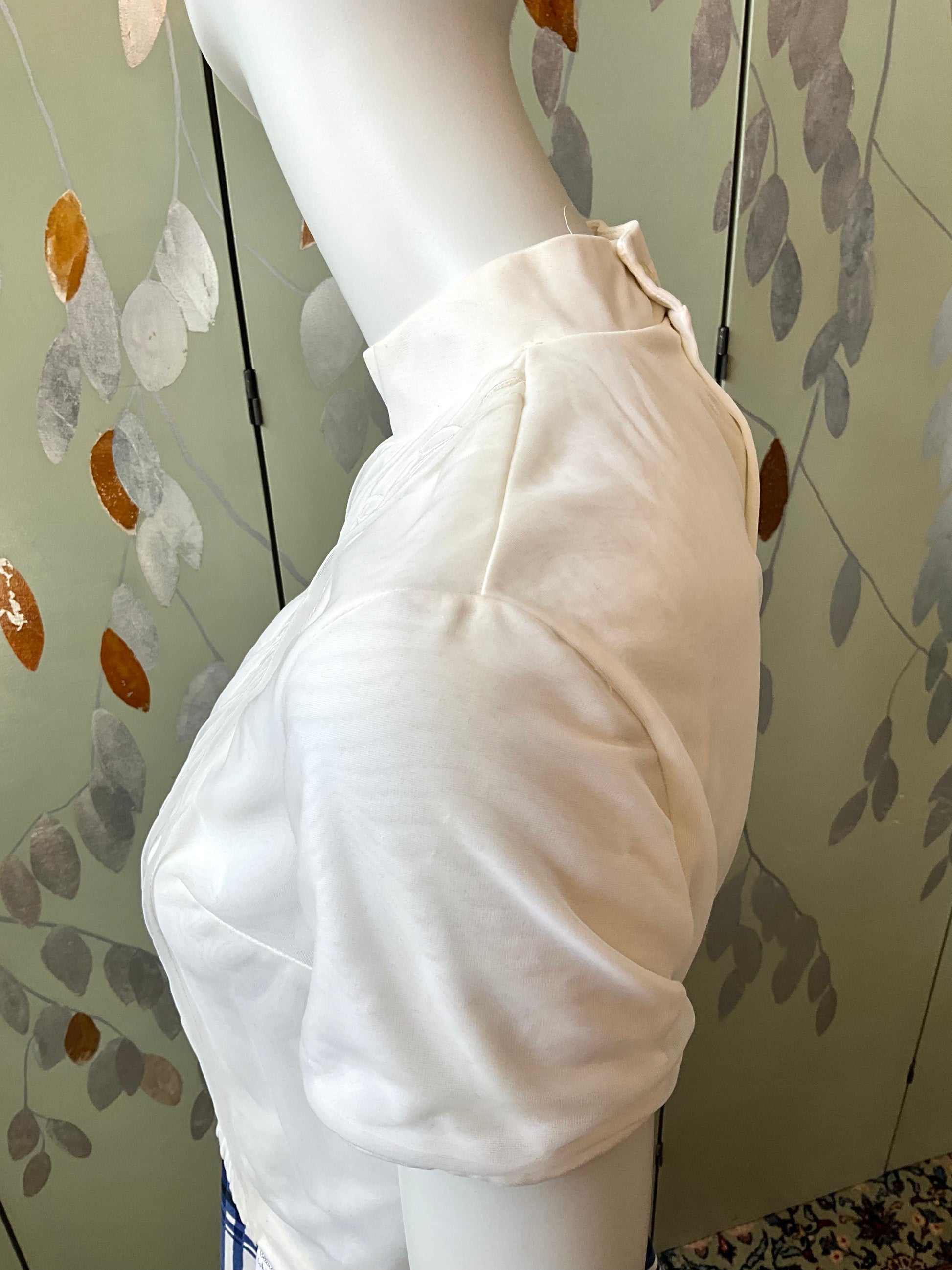 White shirt on a mannequin against a decorative wall.