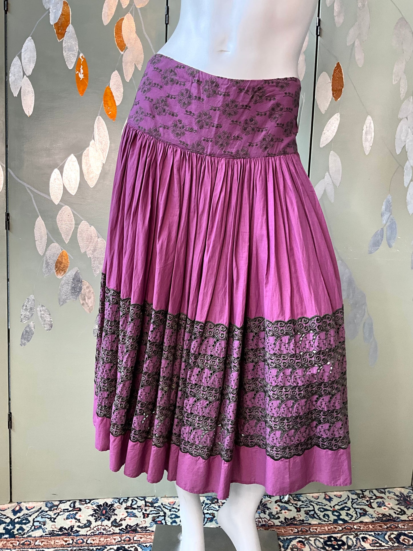 Purple skirt with black lace trim on a mannequin against a decorative wall.