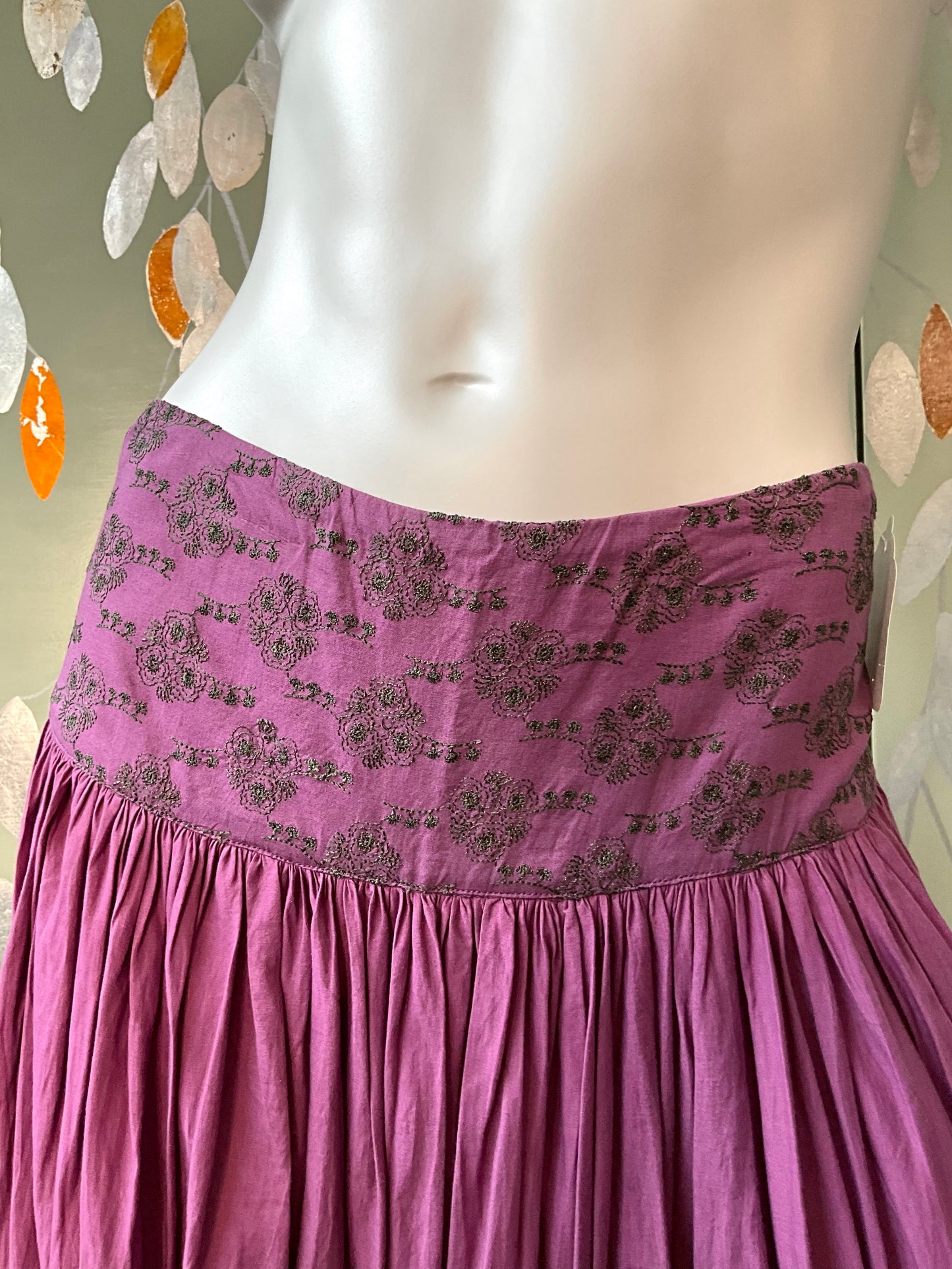 Purple skirt with floral pattern on a mannequin against a decorative wall.