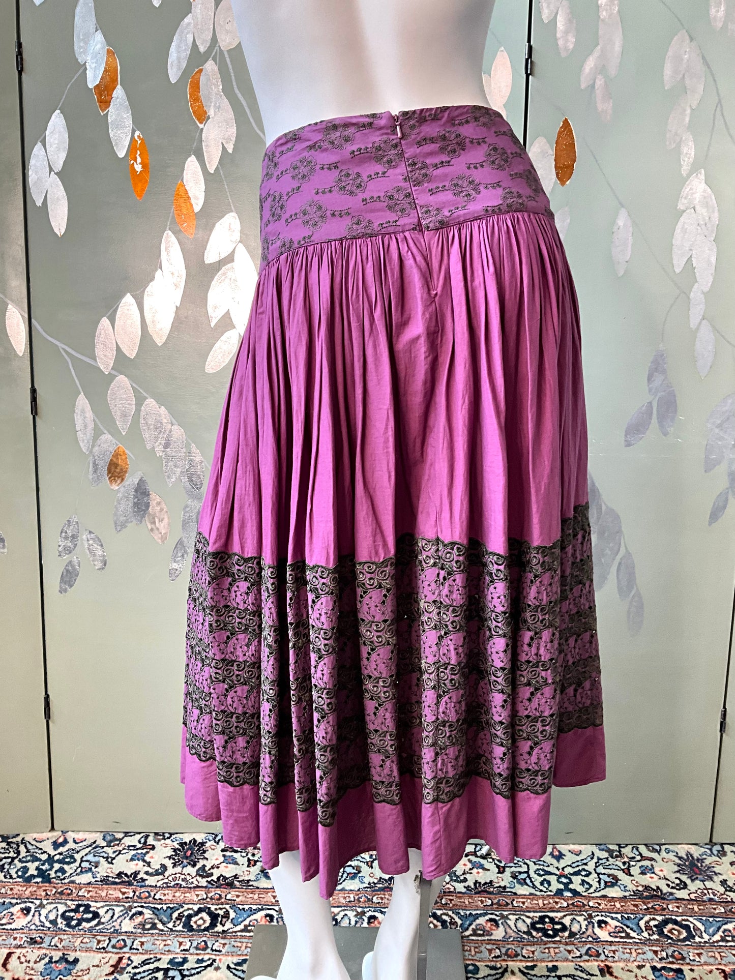 Purple skirt with patterned hem on a mannequin against a decorative wall.