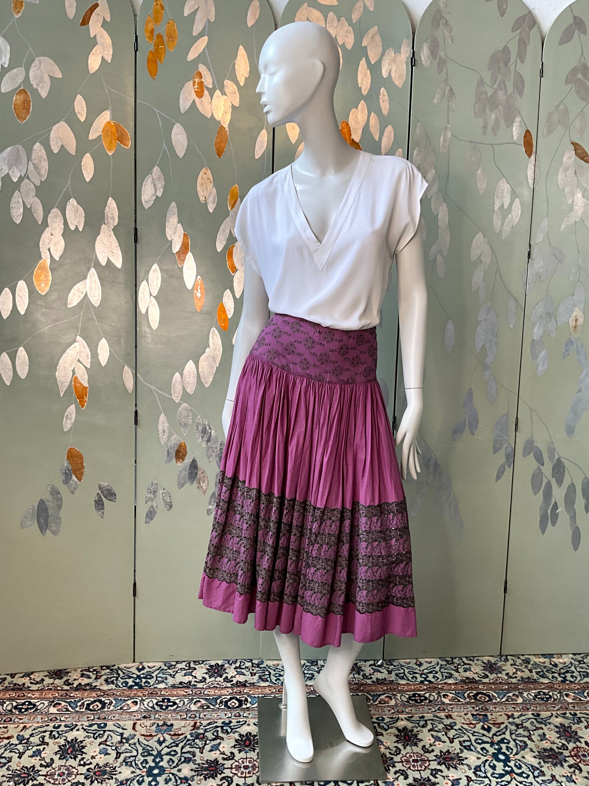 Mannequin wearing a white top and purple skirt with a leaf-patterned background