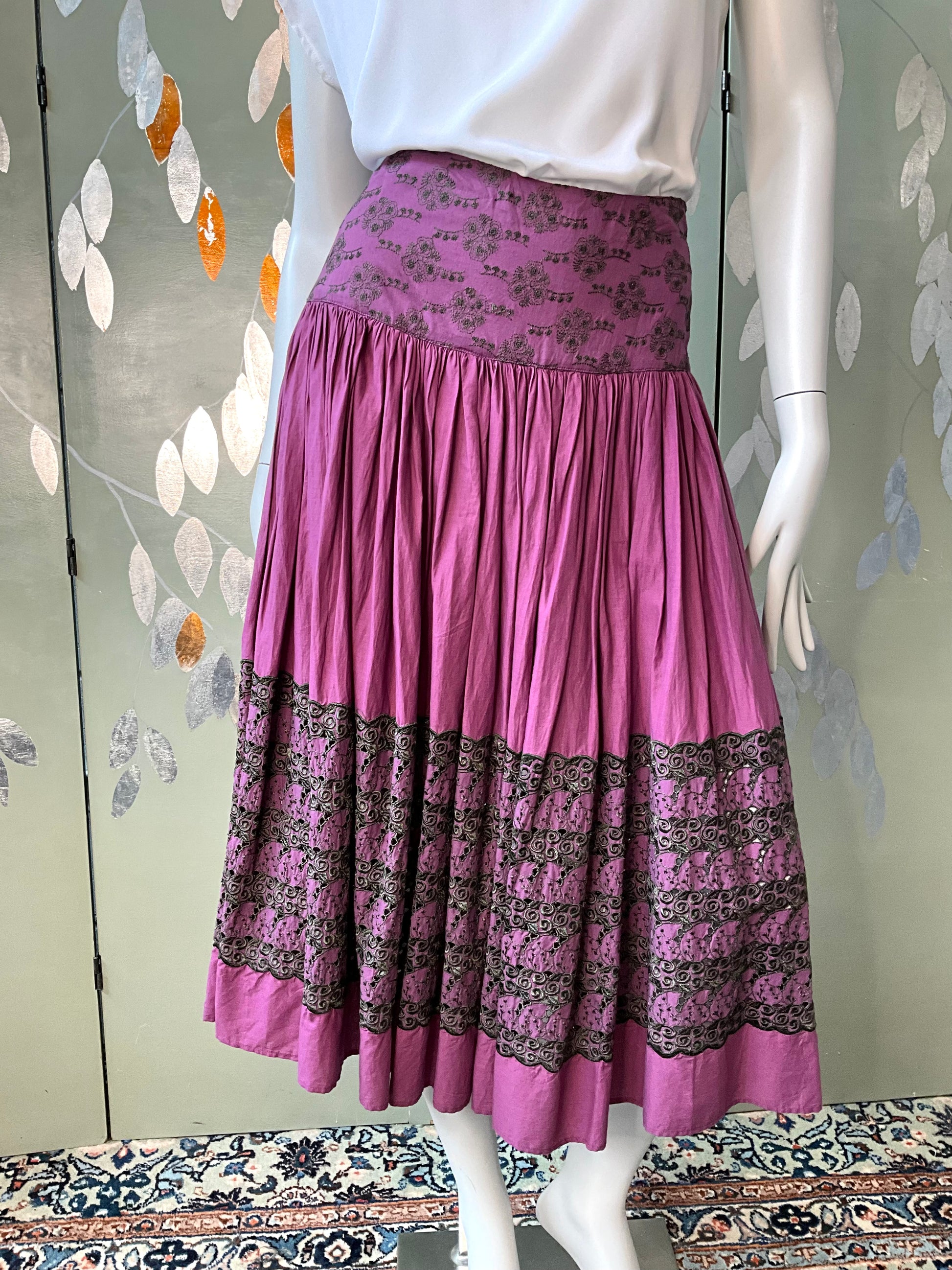 Mannequin wearing a purple skirt with black pattern against a decorative wall.
