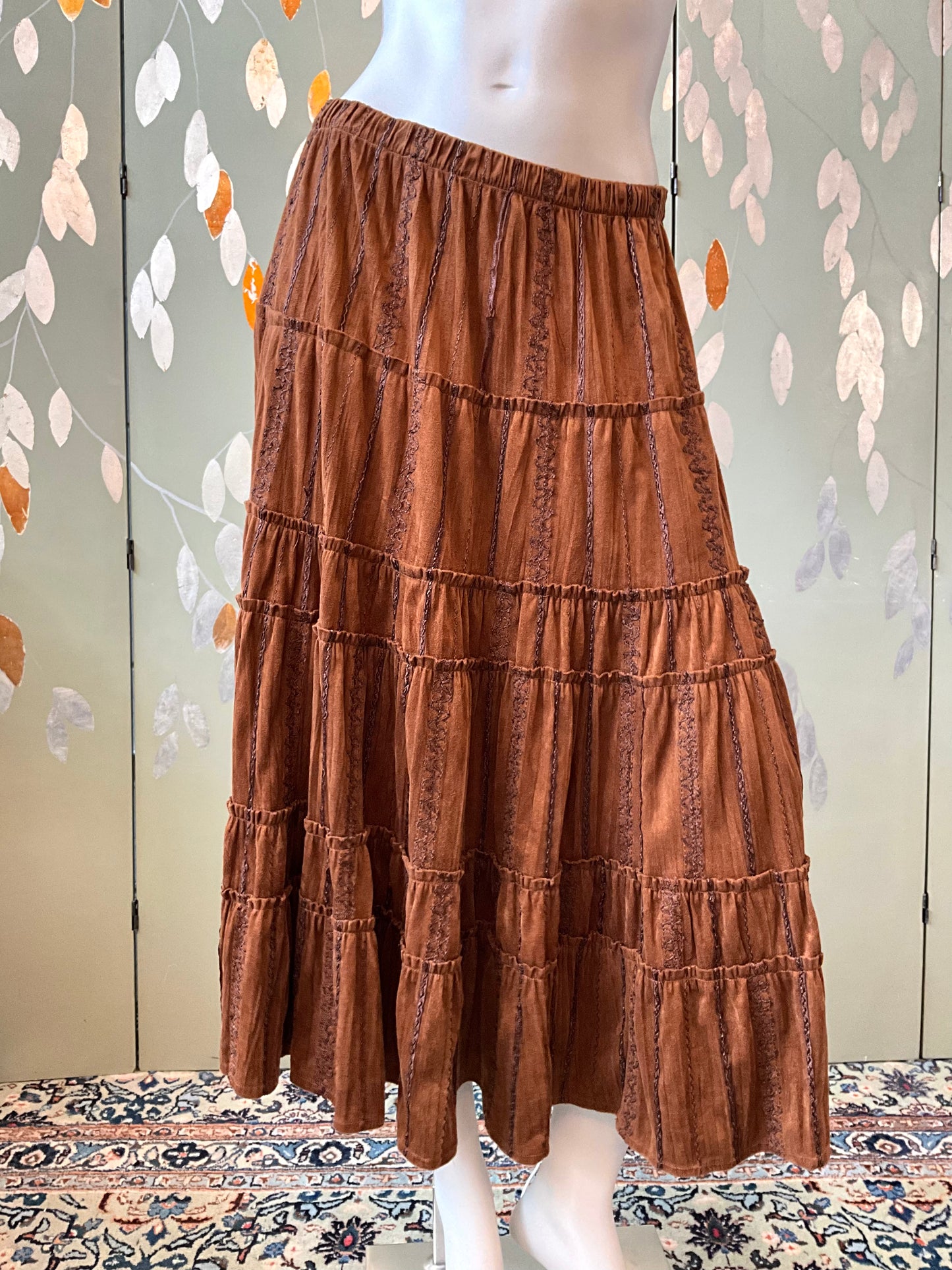 Brown tiered skirt on a mannequin against a decorative wall.