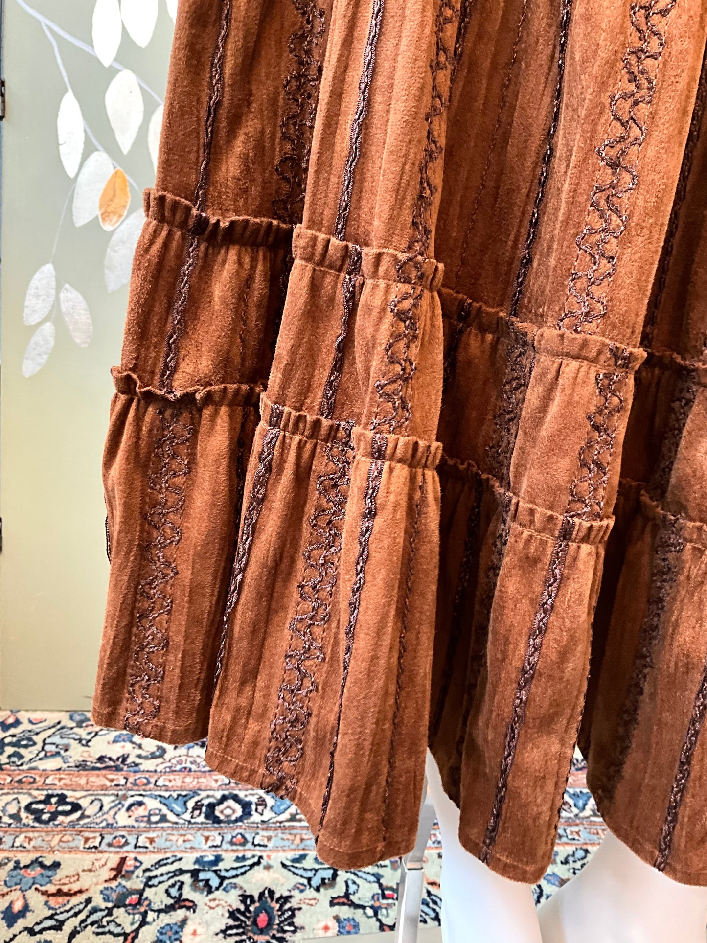 Brown textured fabric with intricate patterns on a mannequin against a floral-patterned rug.