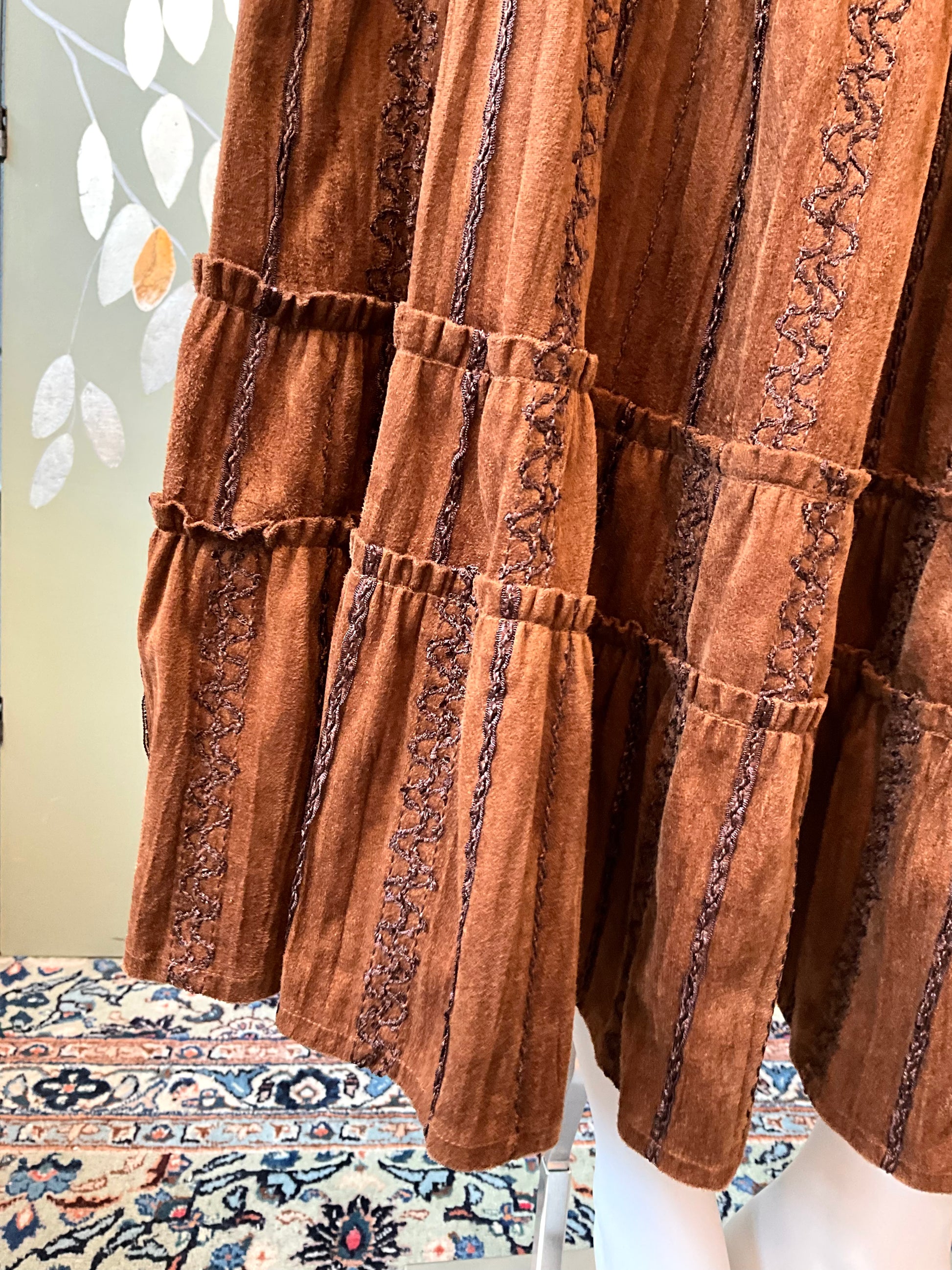 Brown textured fabric with intricate patterns on a mannequin against a floral-patterned rug.