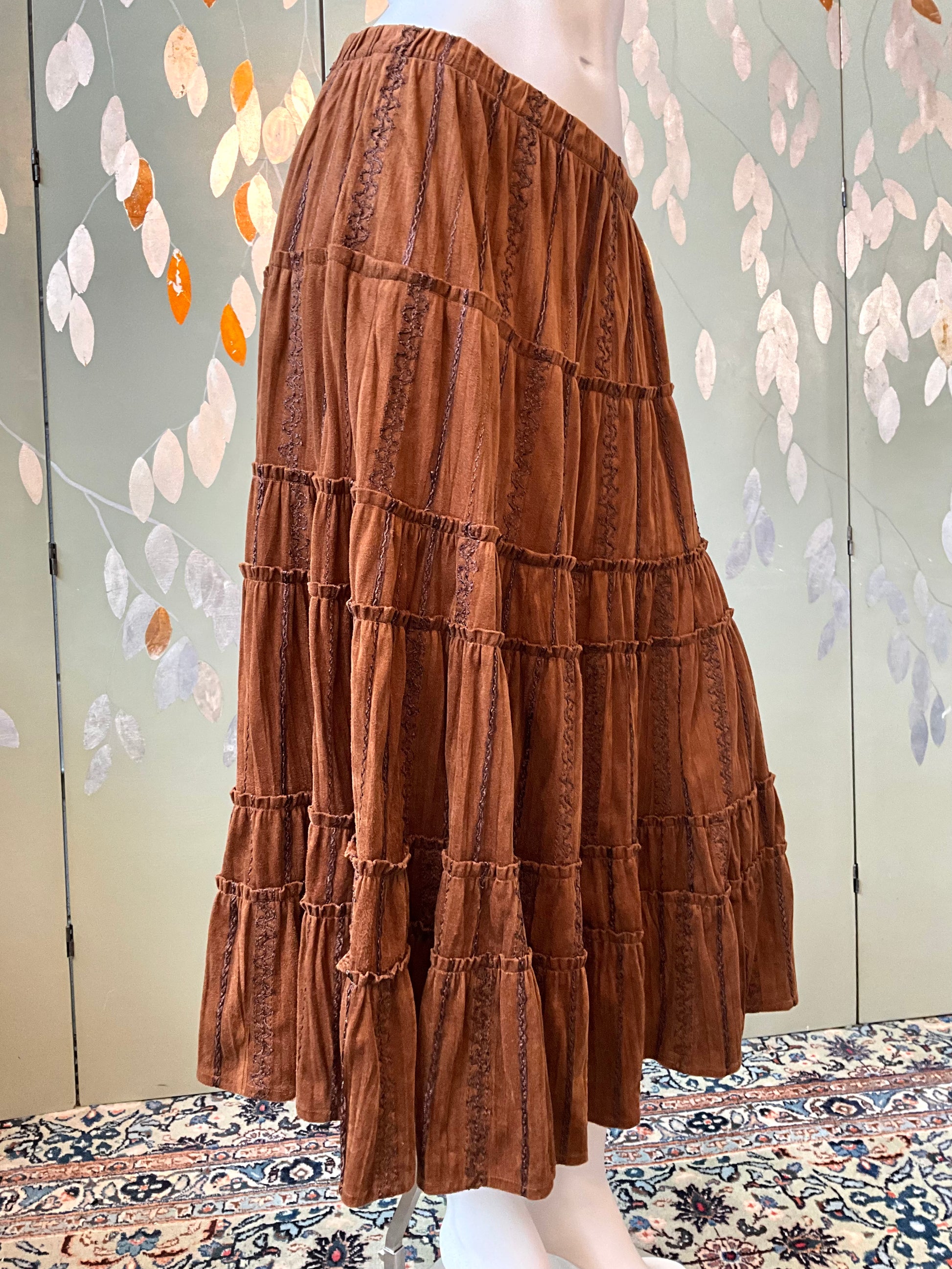 Brown tiered skirt on a mannequin against a decorative wall.