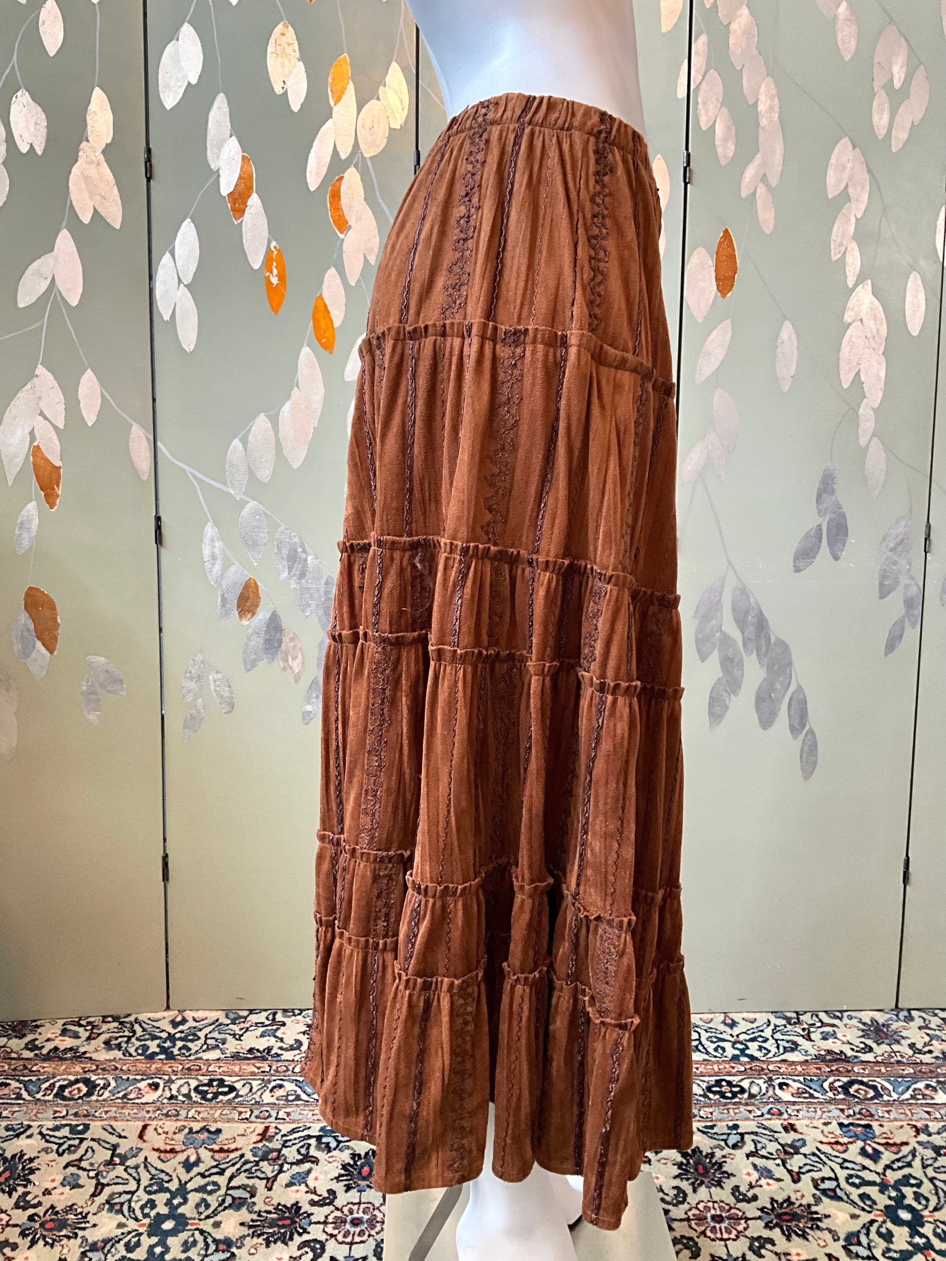 Brown tiered skirt on a mannequin against a decorative wall.