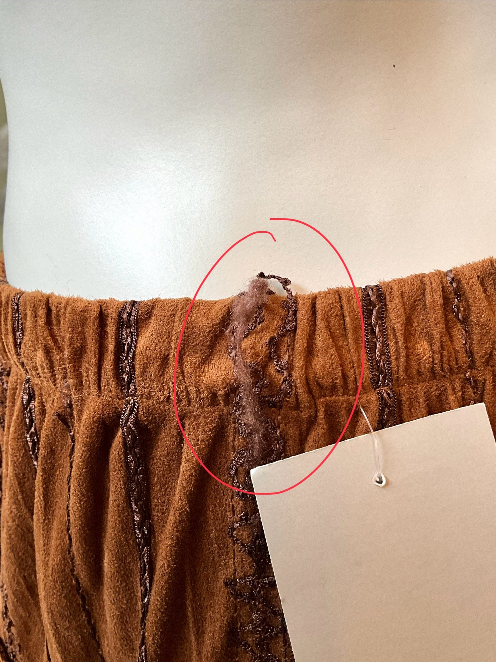 Brown fabric with a red circle highlighting a small defect on a plain background