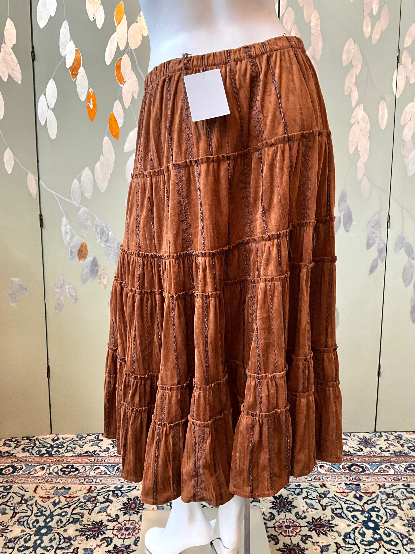 Brown tiered skirt on a mannequin against a decorative wall.