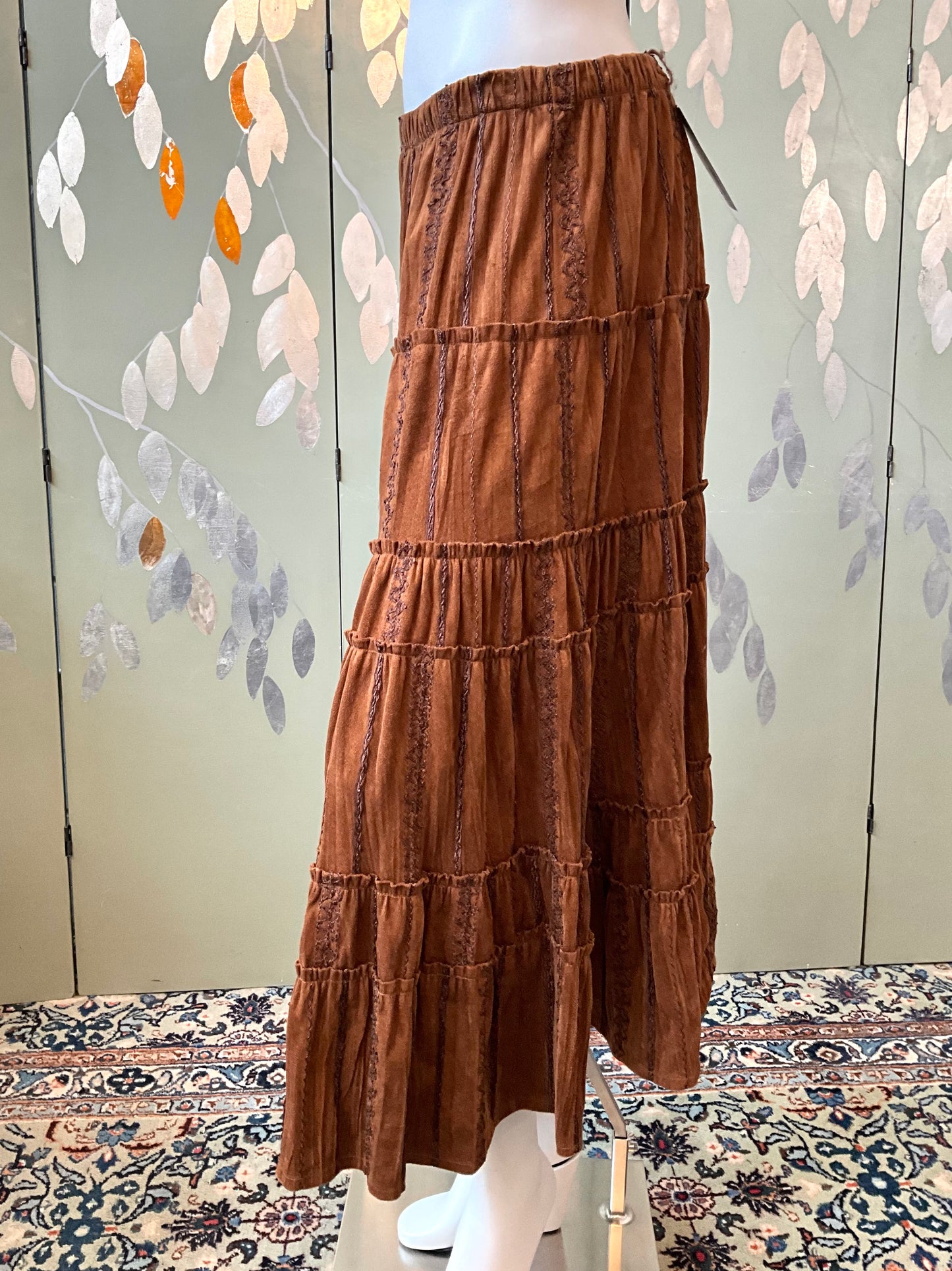 Brown tiered skirt on a mannequin against a decorative wall.