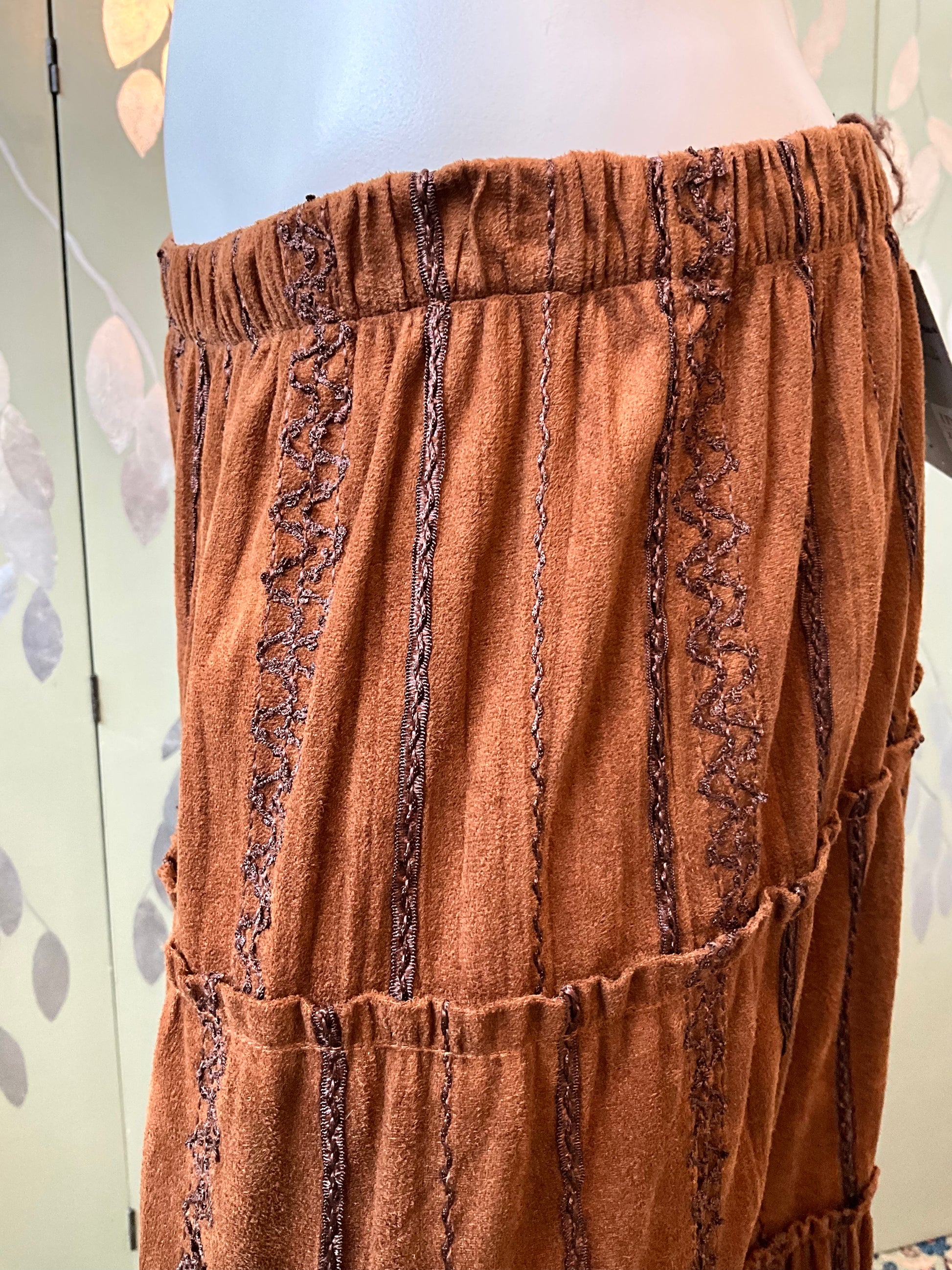 Brown skirt with decorative trim on a mannequin against a neutral background