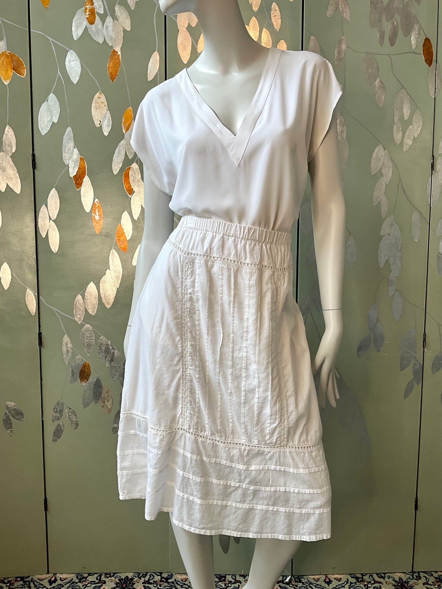 Mannequin wearing a white skirt against a decorative wall.