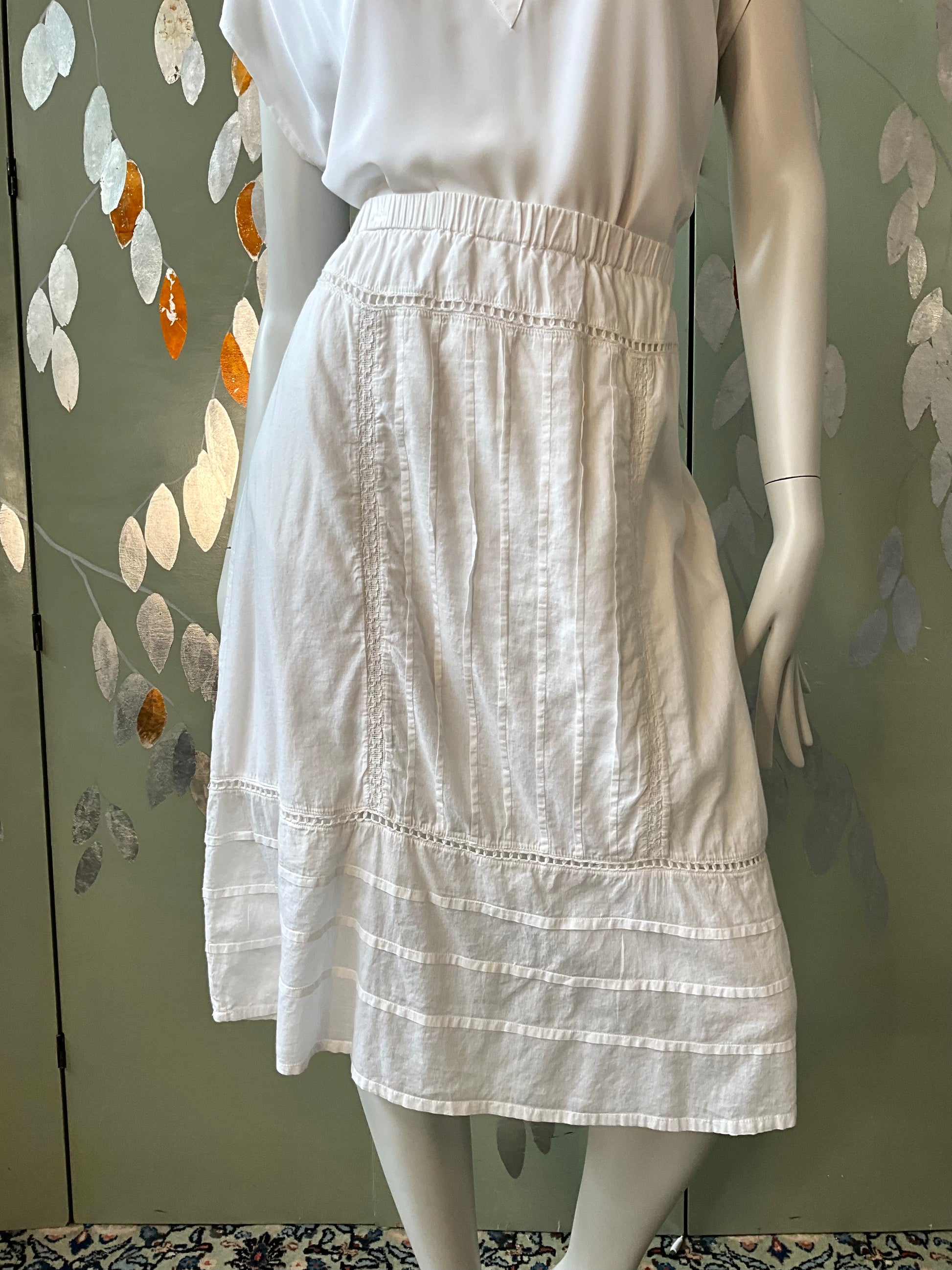 White skirt on a mannequin against a decorative wall.
