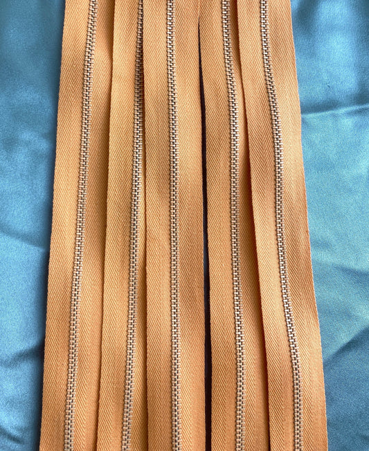 A close-up of a batch of light orange metal vintage zippers. Ian Drummond Vintage. 