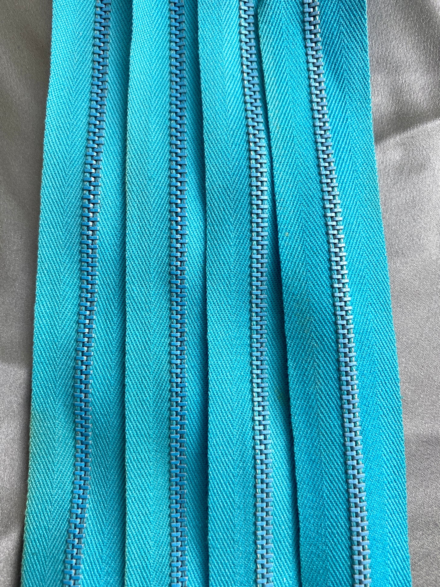Close-up of 4 light blue metal vintage zippers. Ian Drummond Vintage. 