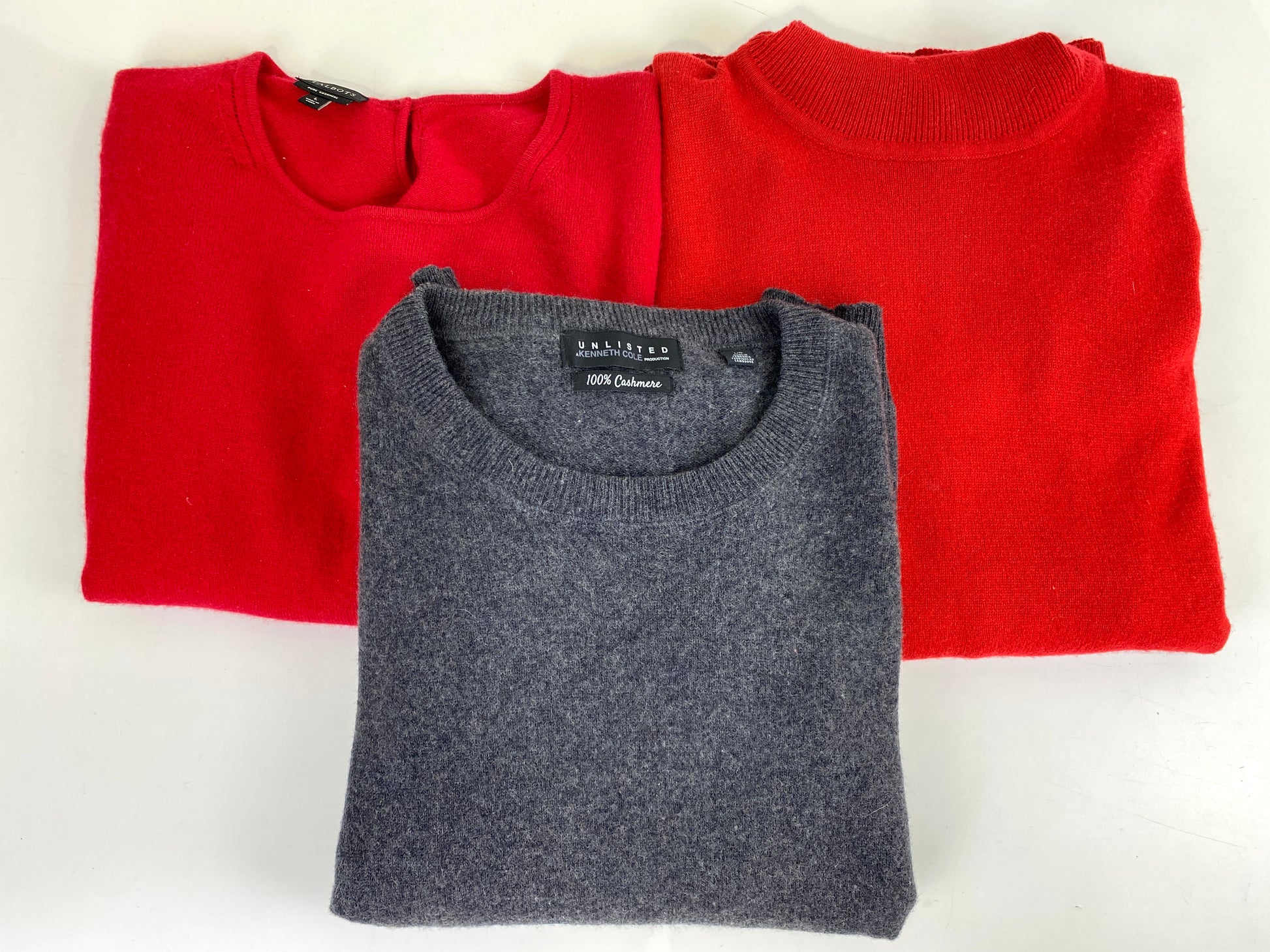 3 cashmere sweaters folded on table. 1 grey and 2 red. Ian Drummond Vintage. 